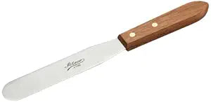 A stainless steel offset spatula with a wooden handle lies on a white surface.
