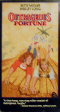 Bette Midler and Shelley Long star in Outrageous Fortune, dodging a helicopter and clutching ropes in a comedic scene from the movie.
