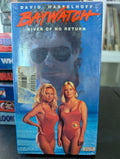 A vintage Baywatch VHS tape cover features David Hasselhoff, Pamela Anderson, and another lifeguard in a red swimsuit against a blue ocean backdrop.
