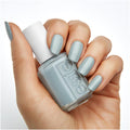 A hand displays Essie brand nail polish, featuring a matching light gray-blue manicure.
