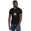 A man models a black H.M.M. Vinyl Records T-shirt and blue jeans while looking to the side.
