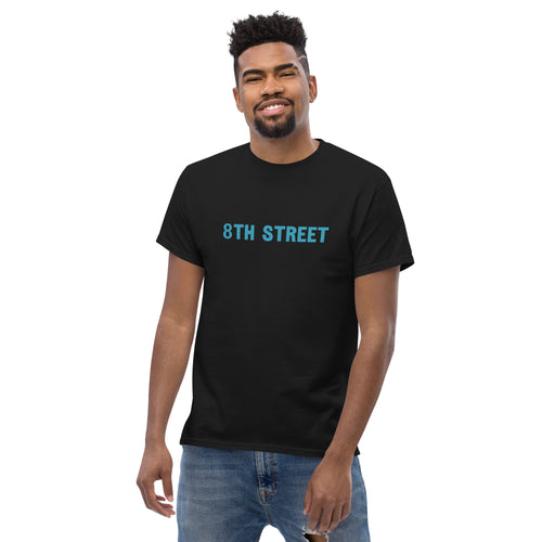 Man smiles while showcasing an 8th Street graphic tee shirt.
