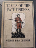 An illustrated cover of "Trails of the Pathfinders" by George Bird Grinnell depicts a frontiersman holding a rifle.
