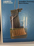 Chemistry textbook cover shows a periodic table partially submerged in a 500ml beaker.
