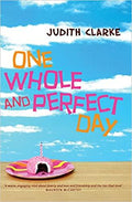 "One Whole and Perfect Day," a novel by Judith Clarke, shows a pink cupcake with a lit candle against a bright blue sky.
